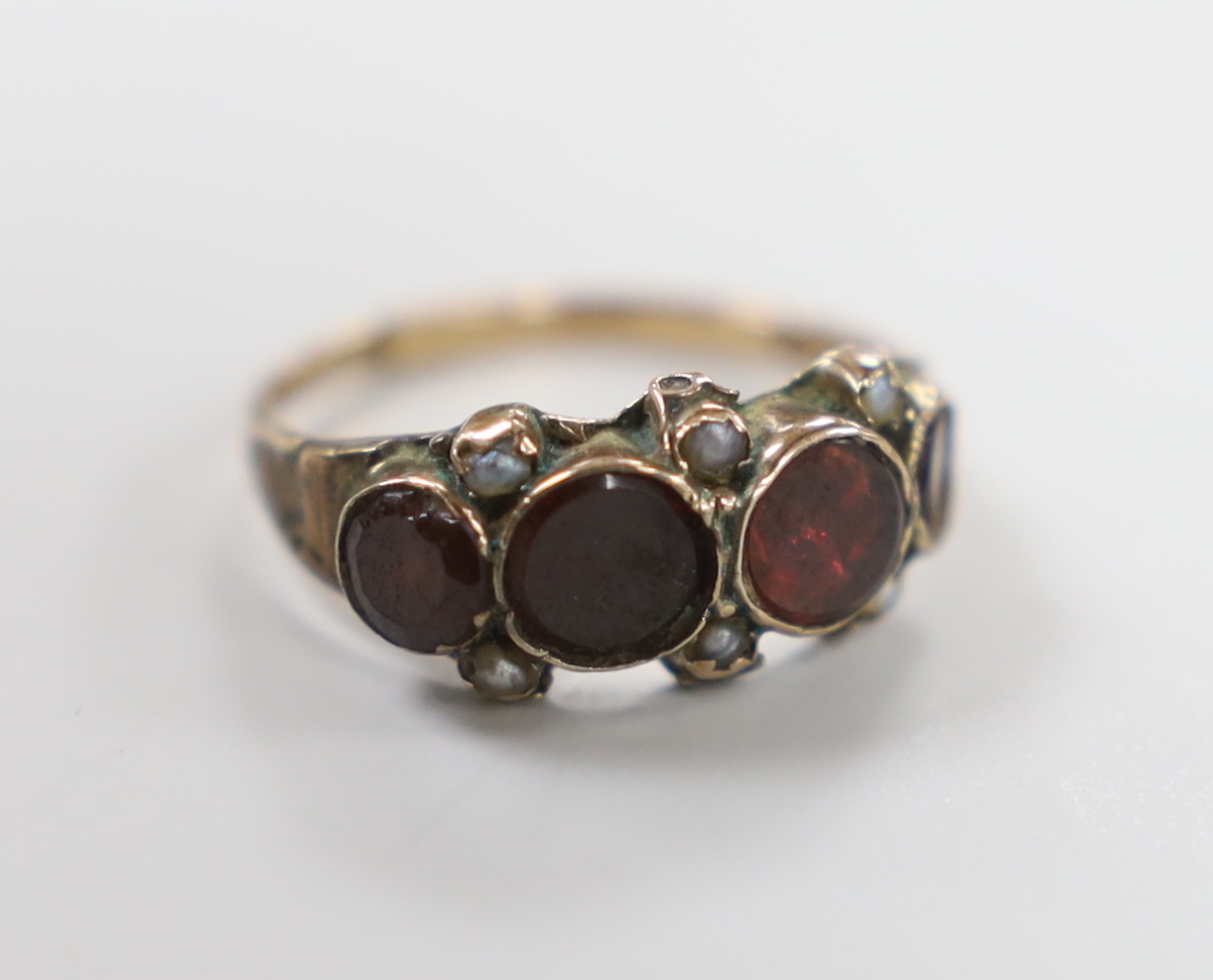 A 19th century yellow metal and graduated four stone foil backed garnet set half hoop ring, with seed pearl spacers, size L, gross weight 1.8 grams, (shank a.f.)